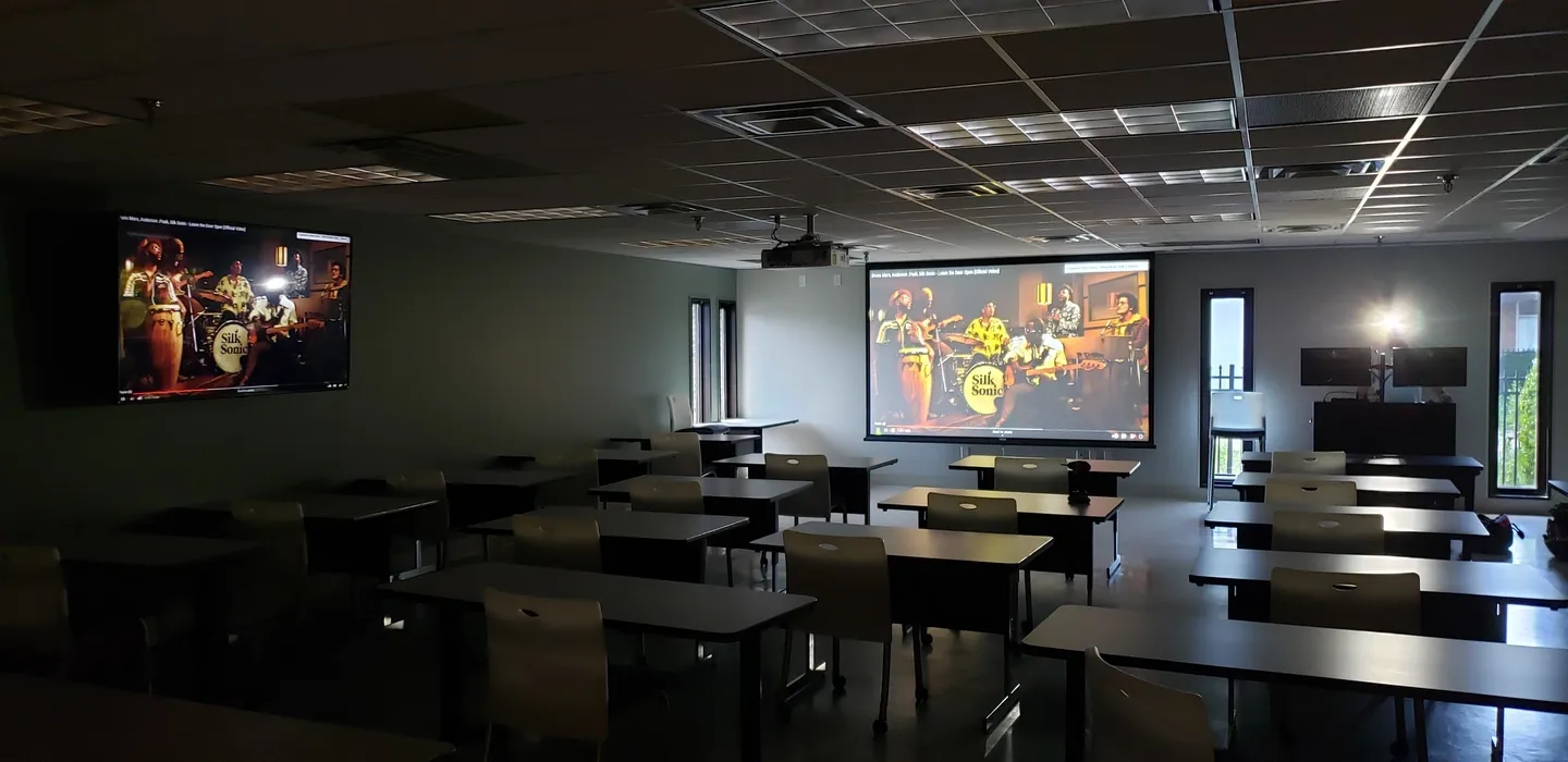 A classroom with tables and chairs, projector screen and ceiling.